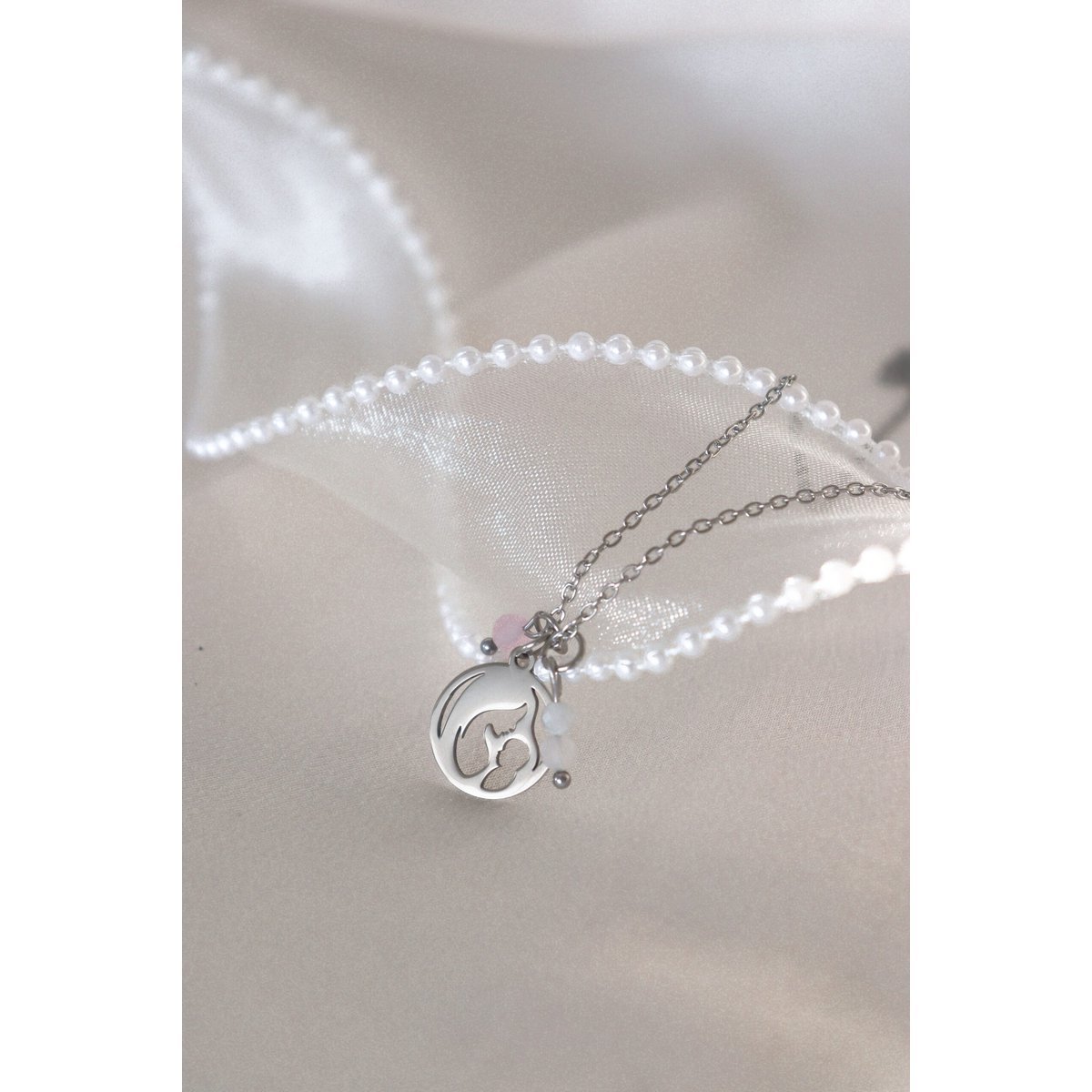 Gouden moeder en baby ketting met rozenkwarts en maansteen op wit satijnen kleed.