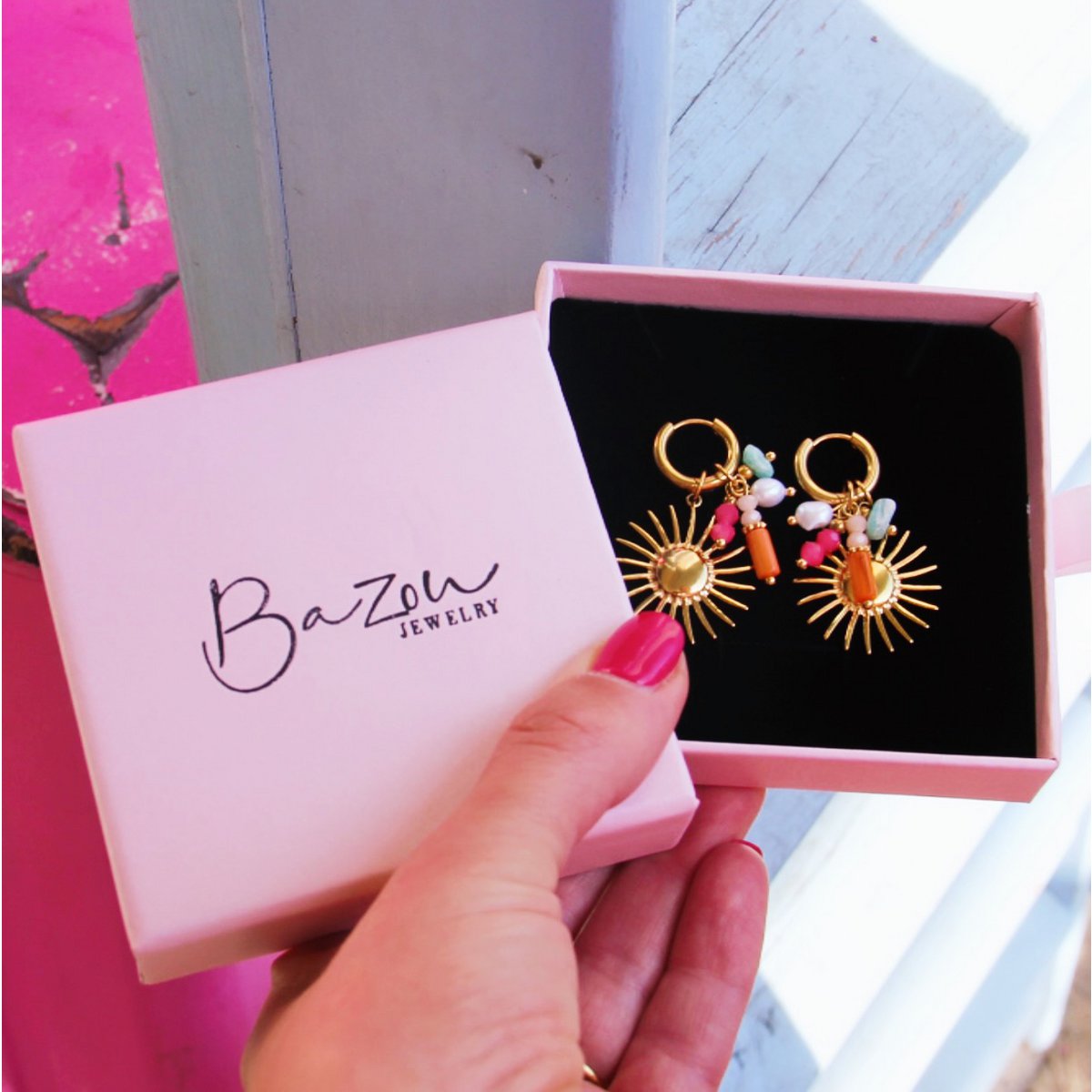 "Gouden RVS zon oorbellen met gekleurde kralen en bedeltjes in een roze Bazou Jewelry geschenkdoosje van Glow Mystic in style."