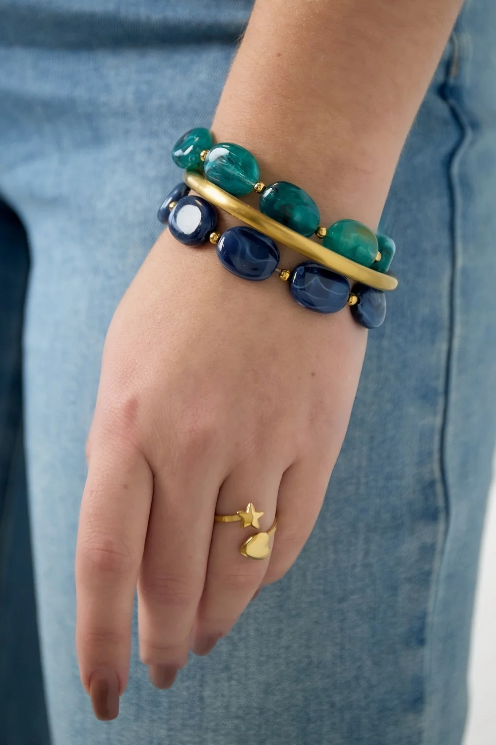 Sfeerbeeld van een armcandy stack om de pols, bestaande uit de groene gemarmerde acryl armband Emerald Swirl, een gouden bangle en een matchende donkerblauwe armband.