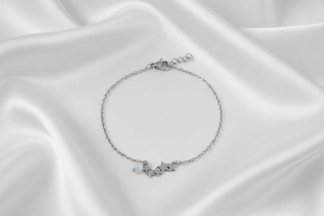 Zilveren stainless steel armband met vijf sterretjes en een witte ronde maansteen kraal op een witte satijnen achtergrond.