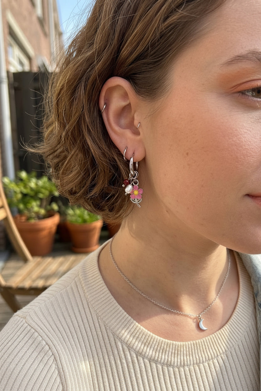 Detailopname van de trendy zilveren waterproof oorbellen met een roze bloem en koraalrood kraaltje voor een zomerse ear party look.