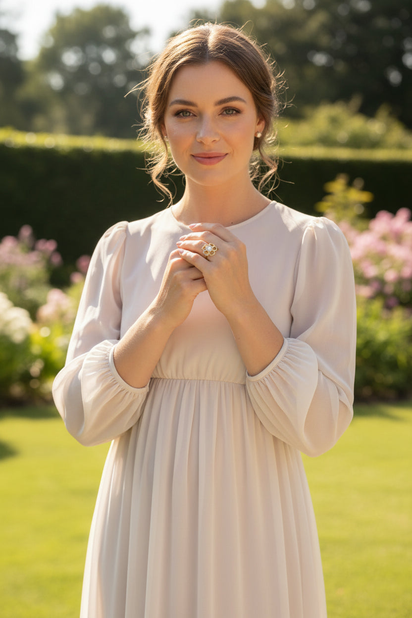 Model in een witte jurk met pofmouwen houdt haar handen gevouwen en draagt een goudkleurige bloemenring met een heldere steen.