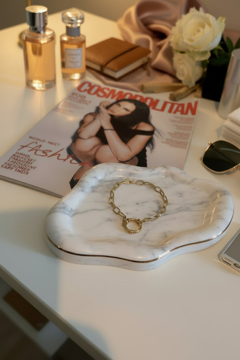 Bedelarmbandje gepresenteerd op een marmeren schaaltje met gouden streep en ligt op een cosmopolitan tijdschrift met parfum, rozen, agenda, bril, en mobiel er omheen gepresenteerd