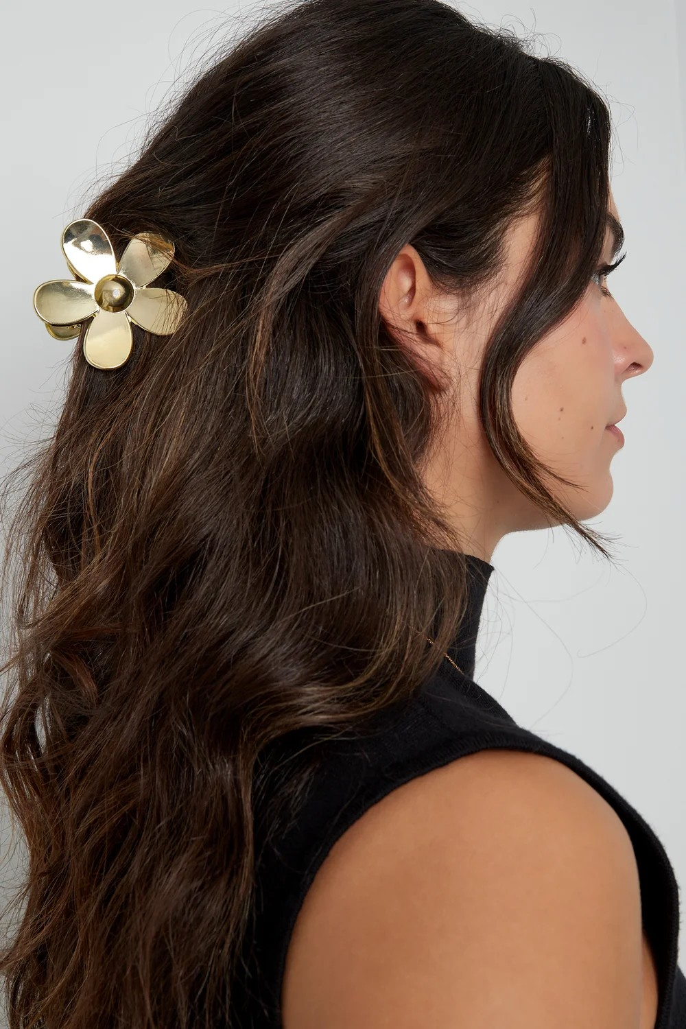 Model van de zijkant met bruin golvend haar waarin een grote gouden bloemen haarklem is bevestigd.