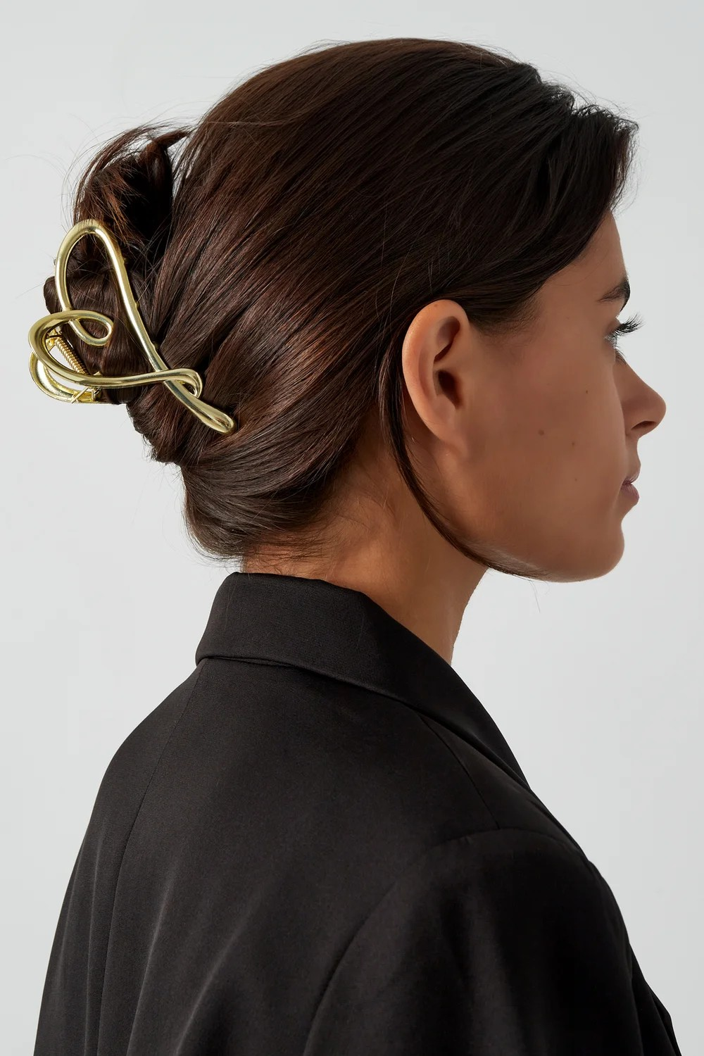 Model van de zijkant met bruin opgestoken haar waarin de grote gouden elegance haarklem is bevestigd.