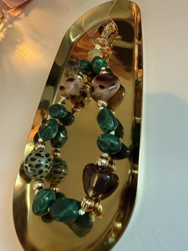 Glow Mystic in Style groene kralen telefoon charm met goudkleurige sluiting op een goudkleurige schaal.