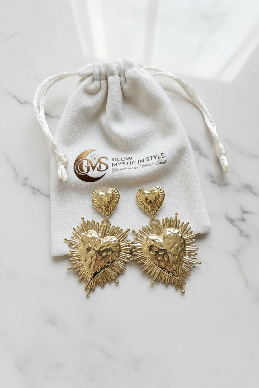 Set van twee goudkleurige RVS statement hart oorbellen gepresenteerd op een wit luxe velvet sieraadzakje met het logo van Glow Mystic in Style.