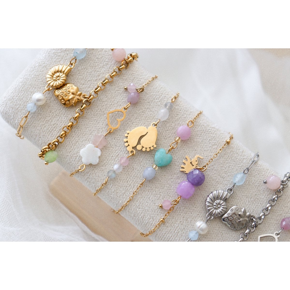 "Gedetailleerde macro-productfoto van het handgemaakte goud RVS geluksarmbandje. De focus ligt op de glanzende olifant-bedel, de geometrische edelsteenkubussen van amethist en lavender jade, en de verfijnde bolletjesketting."
