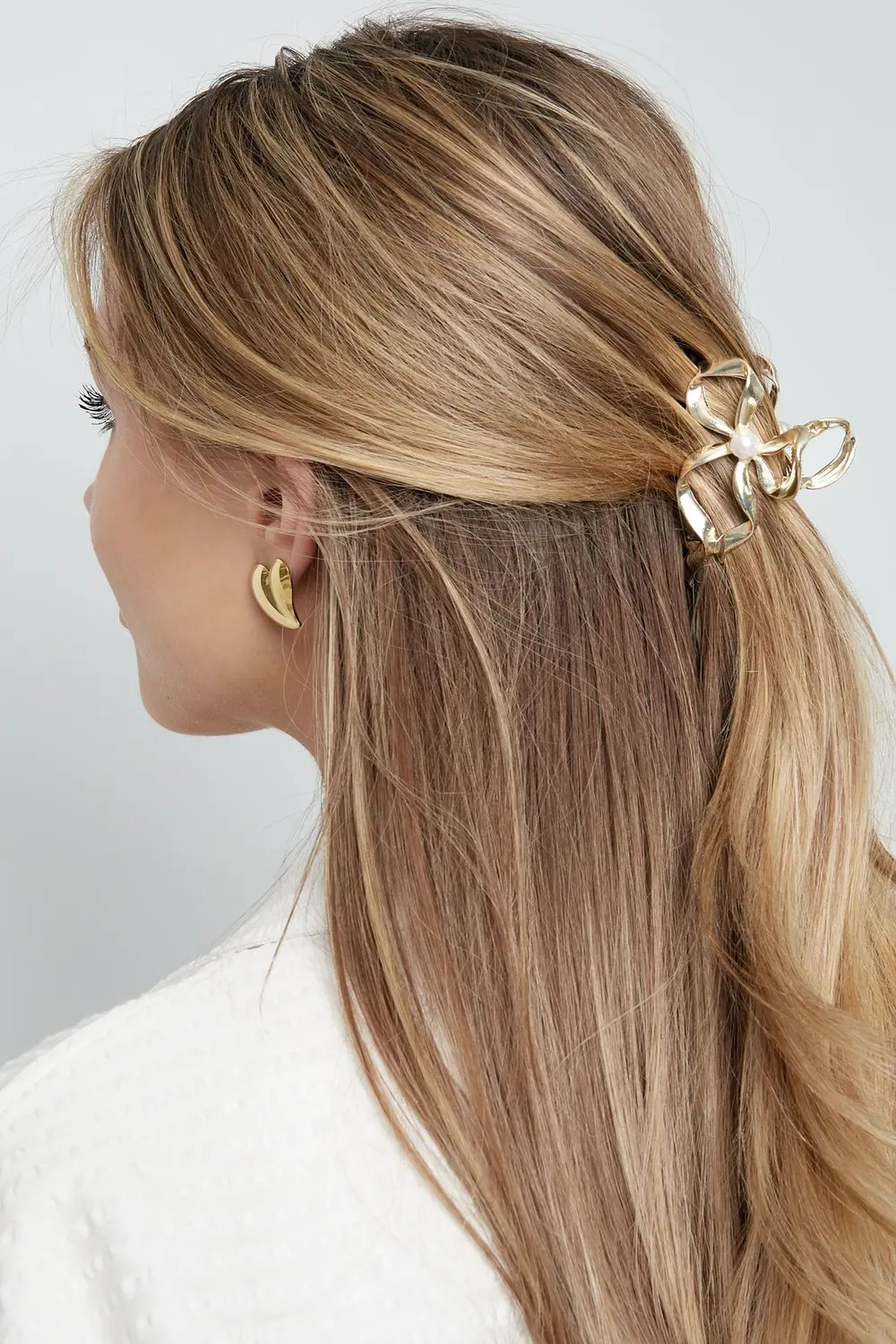 Model van de zijkant met blond haar in een elegante half-up look, vastgezet met de gouden strik haarklem met parel.