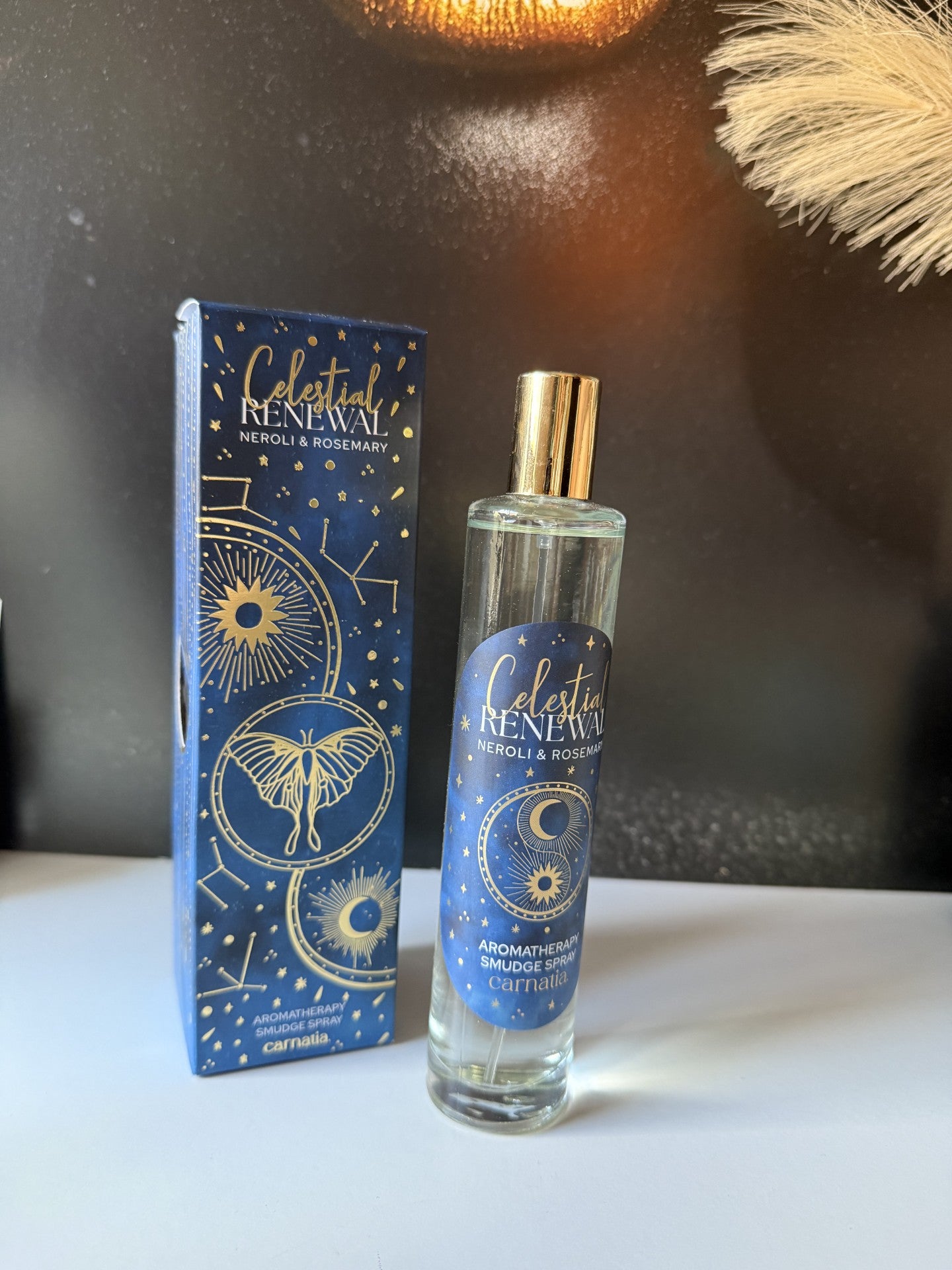 Carnatia Starry Spell Roomspray Celestial Renewal 100ml flacon naast de luxe donkerblauwe verpakking met gouden astrologische details en vlinder - Glow Mystic in Style.