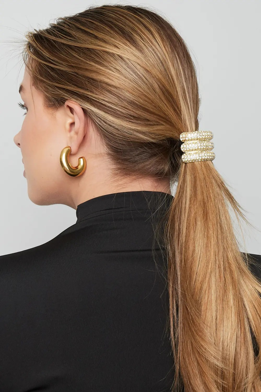 Model van de achterkant met blond haar in een lage paardenstaart, vastgezet met de luxe gouden strass haarstiek elegant glow van Glow Mystic in Style.