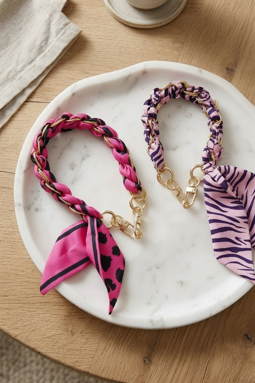 Sfeerbeeld van roze en fuchsia stoffen telefoonkoorden met goudkleurige schakels op een witte marmeren schaal.