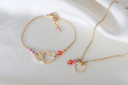 Gouden hartjesketting met edelstenen, gefotografeerd op een wit satijnen kleed.