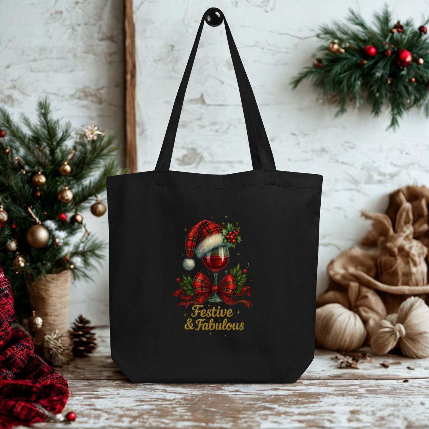 Black Eco Tote Bag with festive holiday design and "Festive & Fabulous" text hanging in cozy Christmas setting
