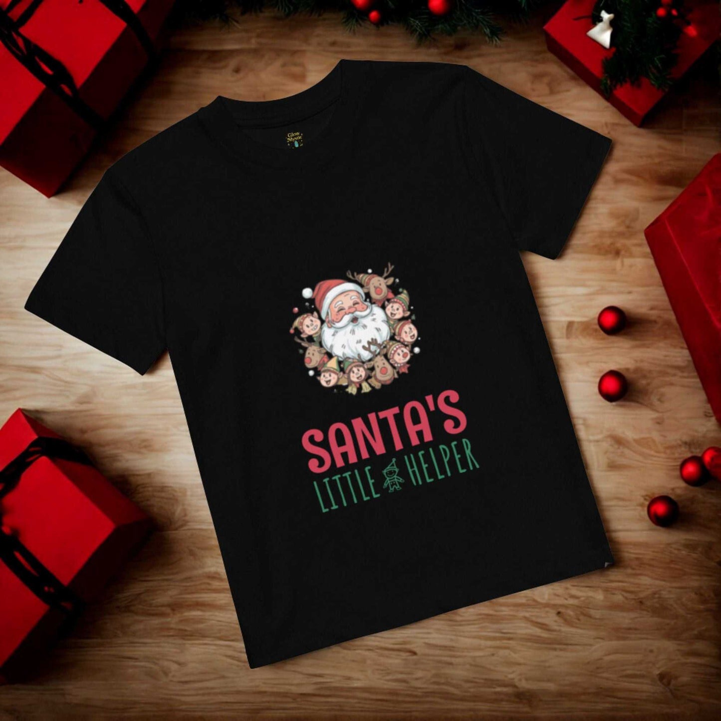 Black Santa's Little Helper Christmas T-Shirt with festive Santa and reindeer design surrounded by red and green holiday decorations on wooden floor