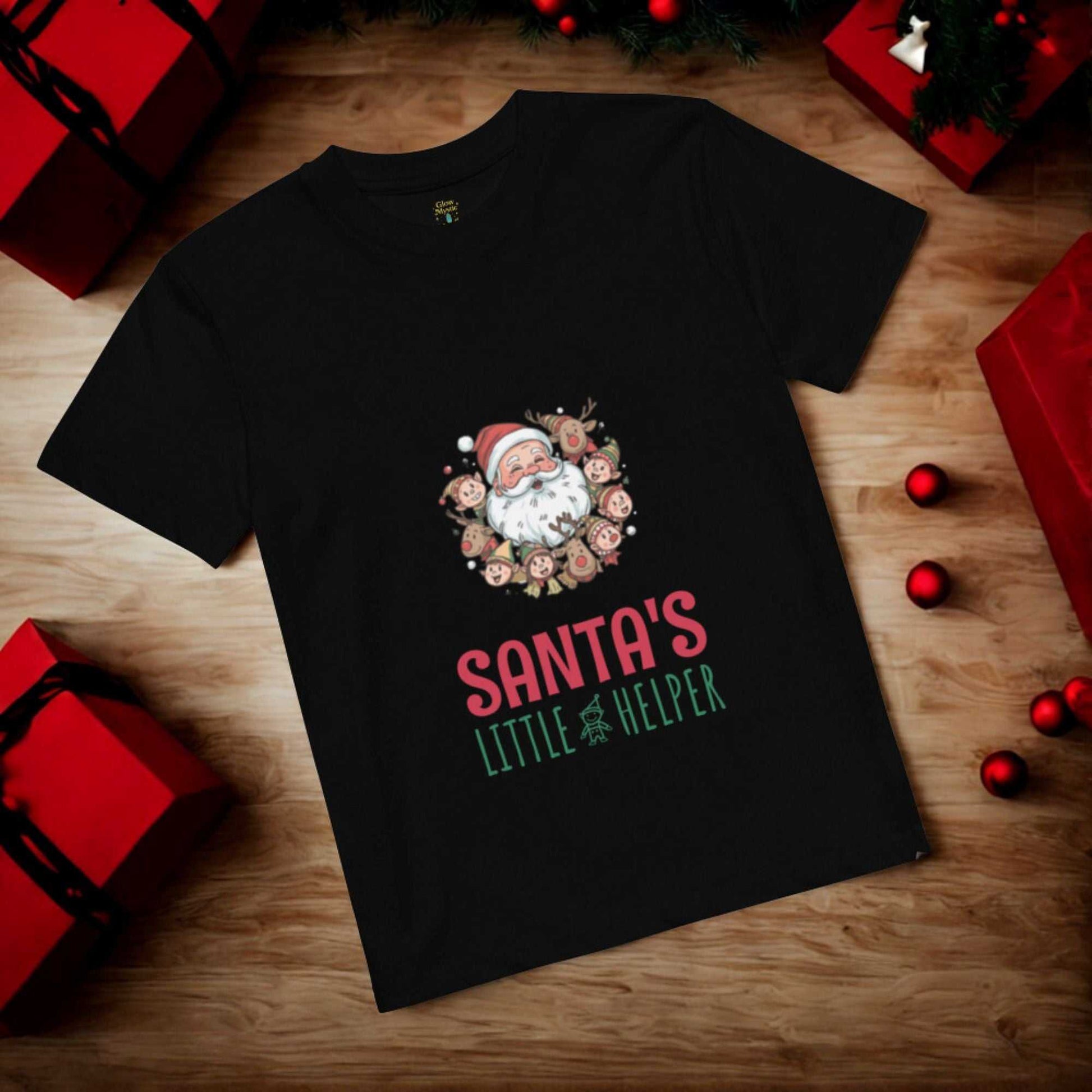 Black Santa's Little Helper Christmas T-Shirt with festive Santa and reindeer design surrounded by red and green holiday decorations on wooden floor