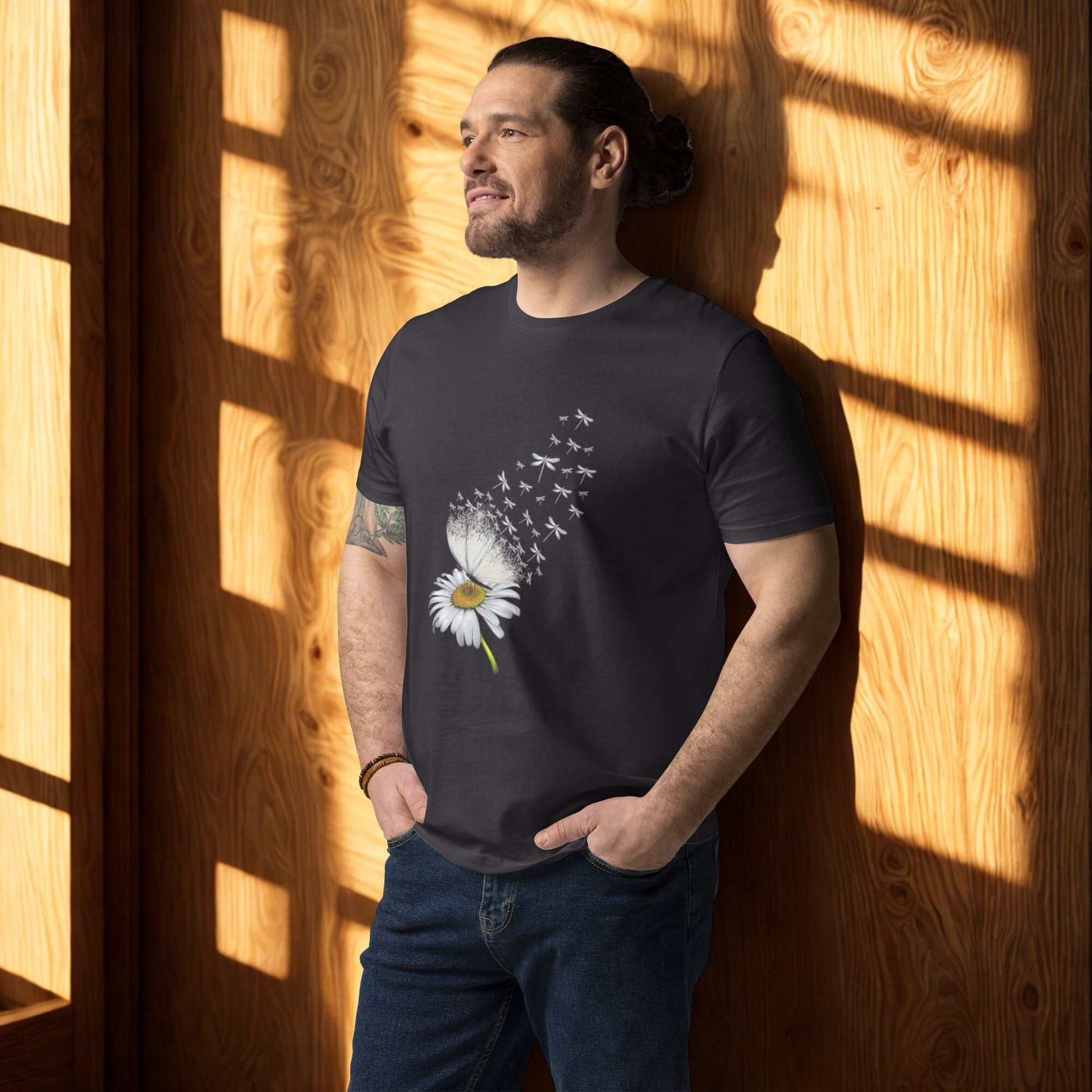 Man wearing black Bloom & Fly Mystic Daisy Organic Cotton Tee with floral design standing by wooden wall in sunlight