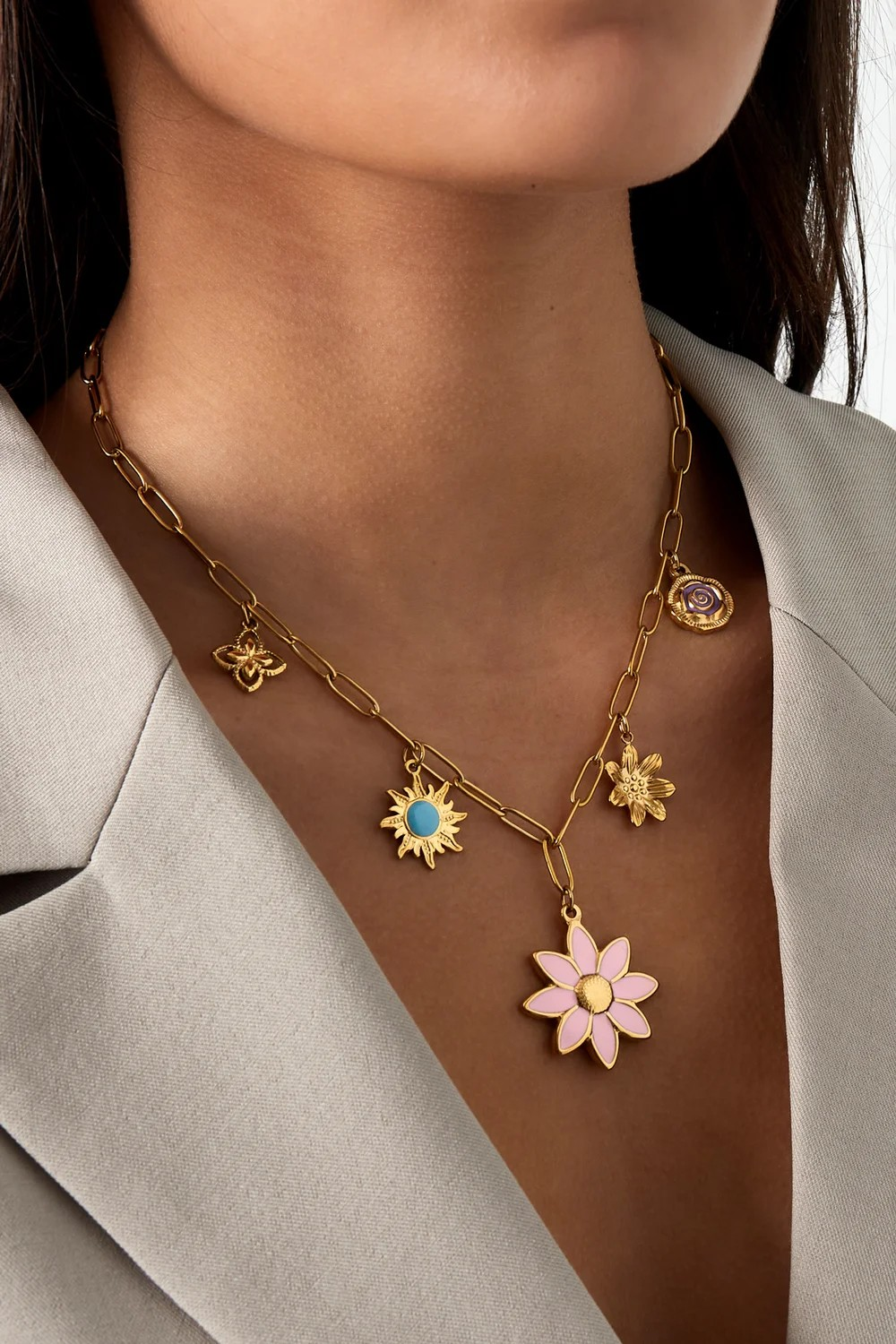 Bloom & Blink gouden RVS bedelketting met roze bloem, turquoise zon en kleurrijke emaille bedels gedragen door een model.