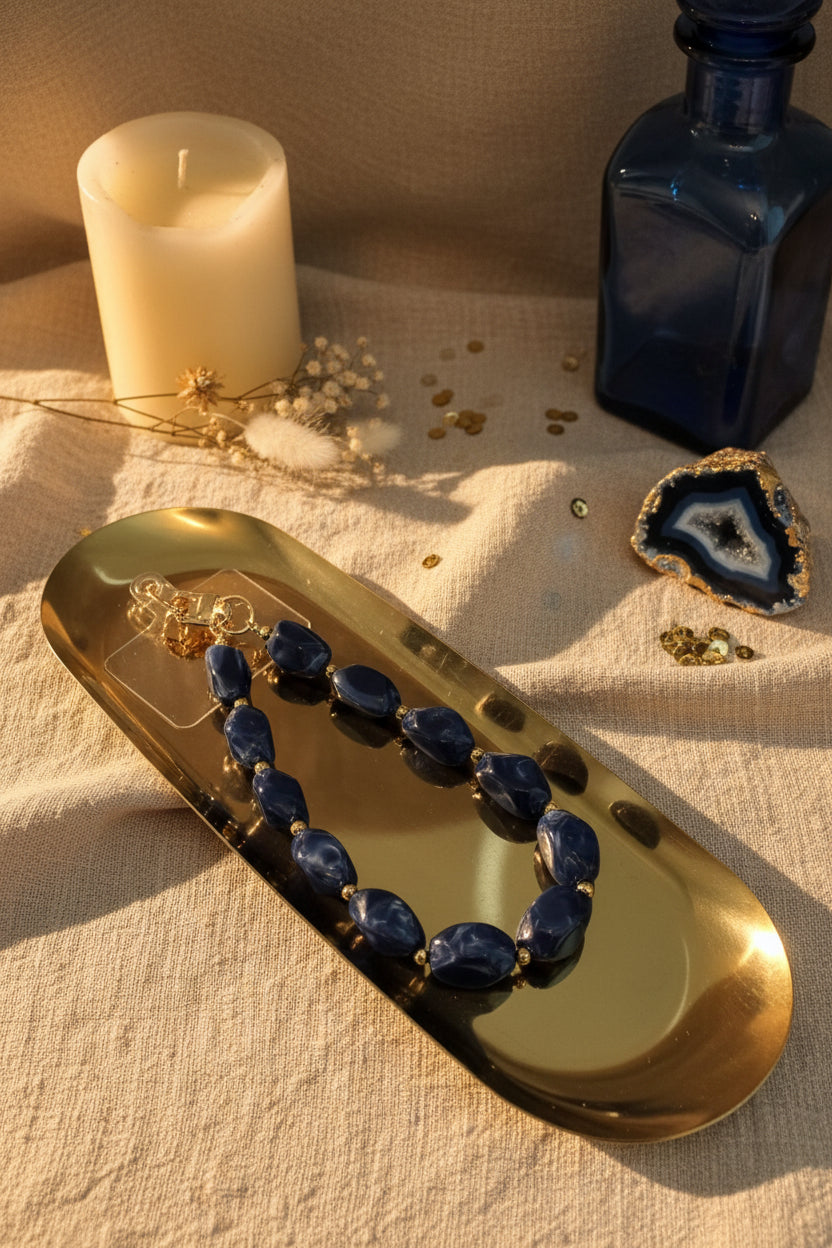 Glow mystic in Style Blauwe kralen telefoonkoord met gouden details op een goudkleurige schaal met lifestyle producten eromheen.
