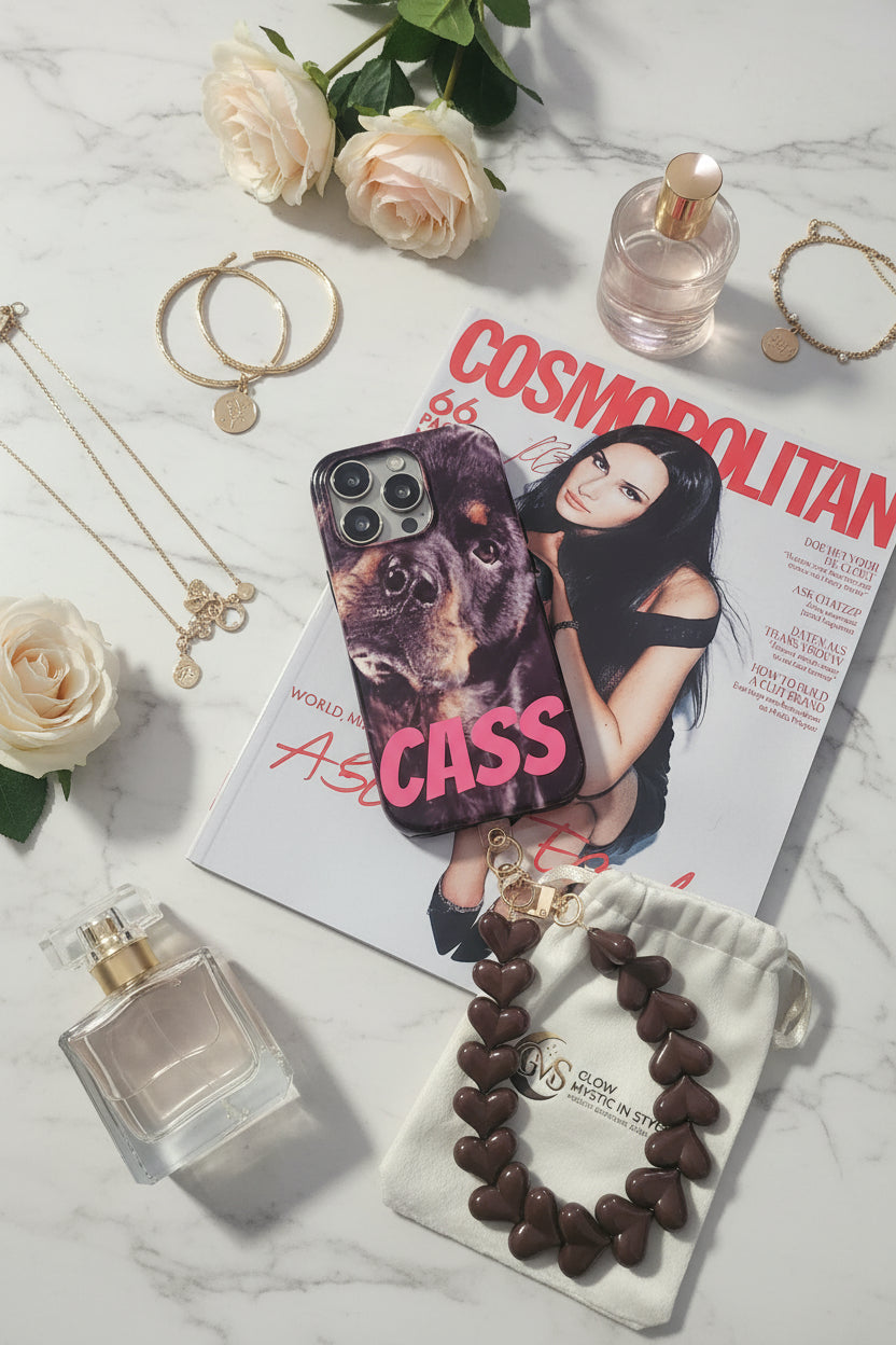 Bruin hartjes telefoonkoord naast smartphone op Cosmopolitan magazine met parfum, sieraden en Glow Mystic in Style sieradenzakje.