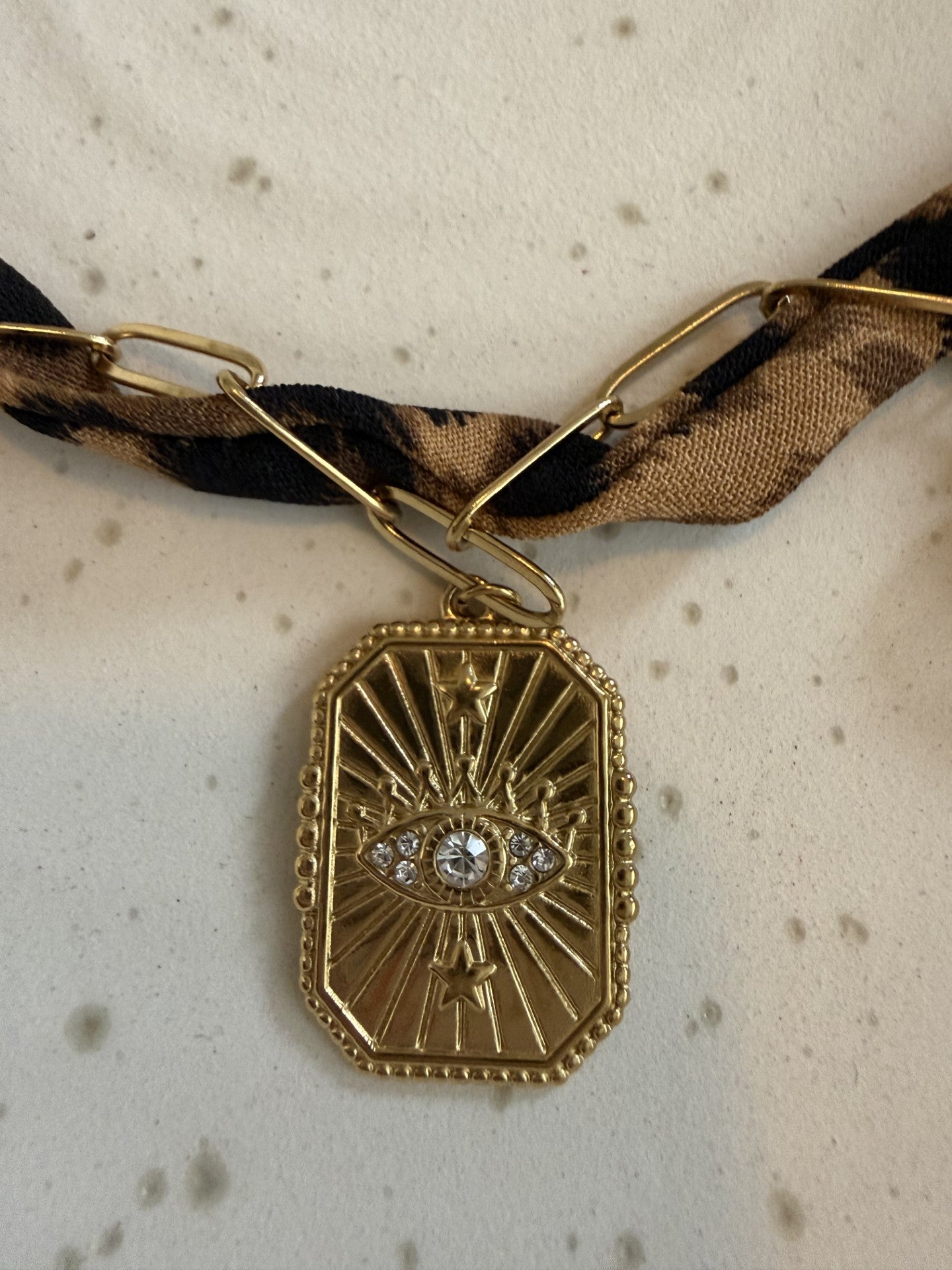 "Gedetailleerde close-up van de bedel aan de panterprint choker: een goudkleurige Evil Eye hanger.