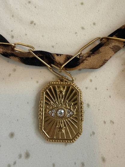 "Gedetailleerde close-up van de bedel aan de panterprint choker: een goudkleurige Evil Eye hanger.