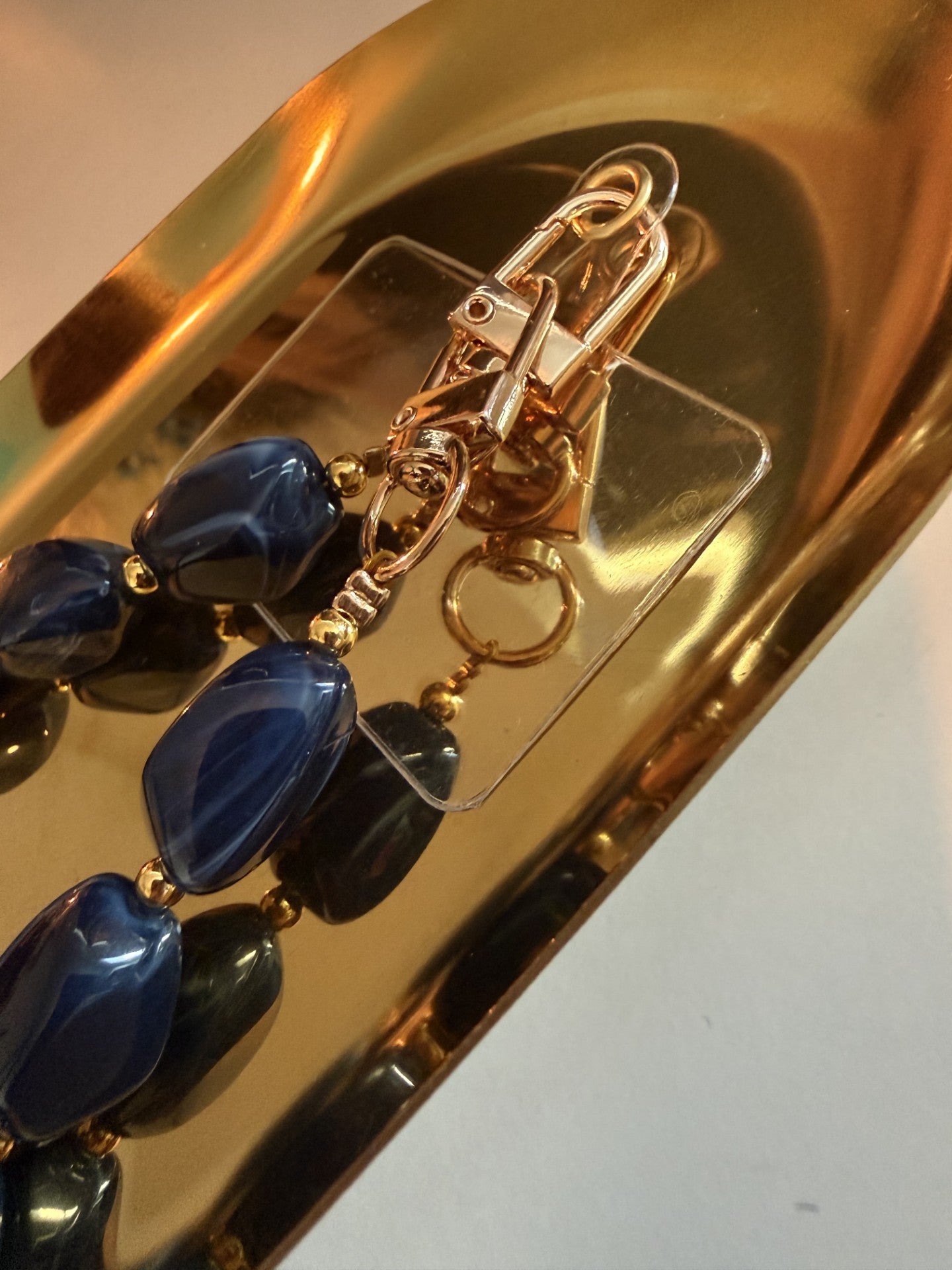 Close upvGlow Mystic in Style luxe marineblauwe kralen telefoonketting op goudkleurige schaal.