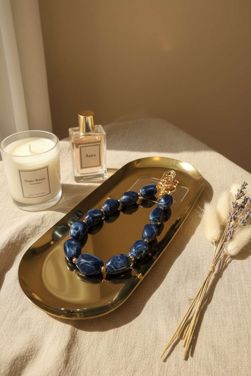 Glow Mystic in Style luxe marineblauwe kralen telefoonketting op goudkleurige schaal met zwart marmeren achtergrond.