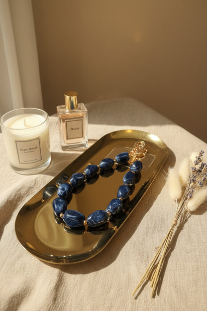 Glow Mystic in Style luxe marineblauwe kralen telefoonketting op goudkleurige schaal met zwart marmeren achtergrond.