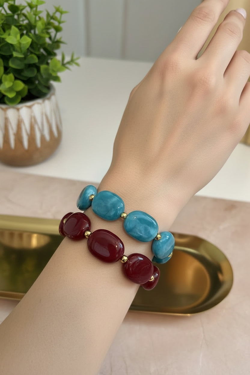 Sfeerbeeld van een armcandy stack om de pols, bestaande uit de groene gemarmerde acryl armband Emerald Swirl, een gouden bangle en een matchende wijnrode armband.