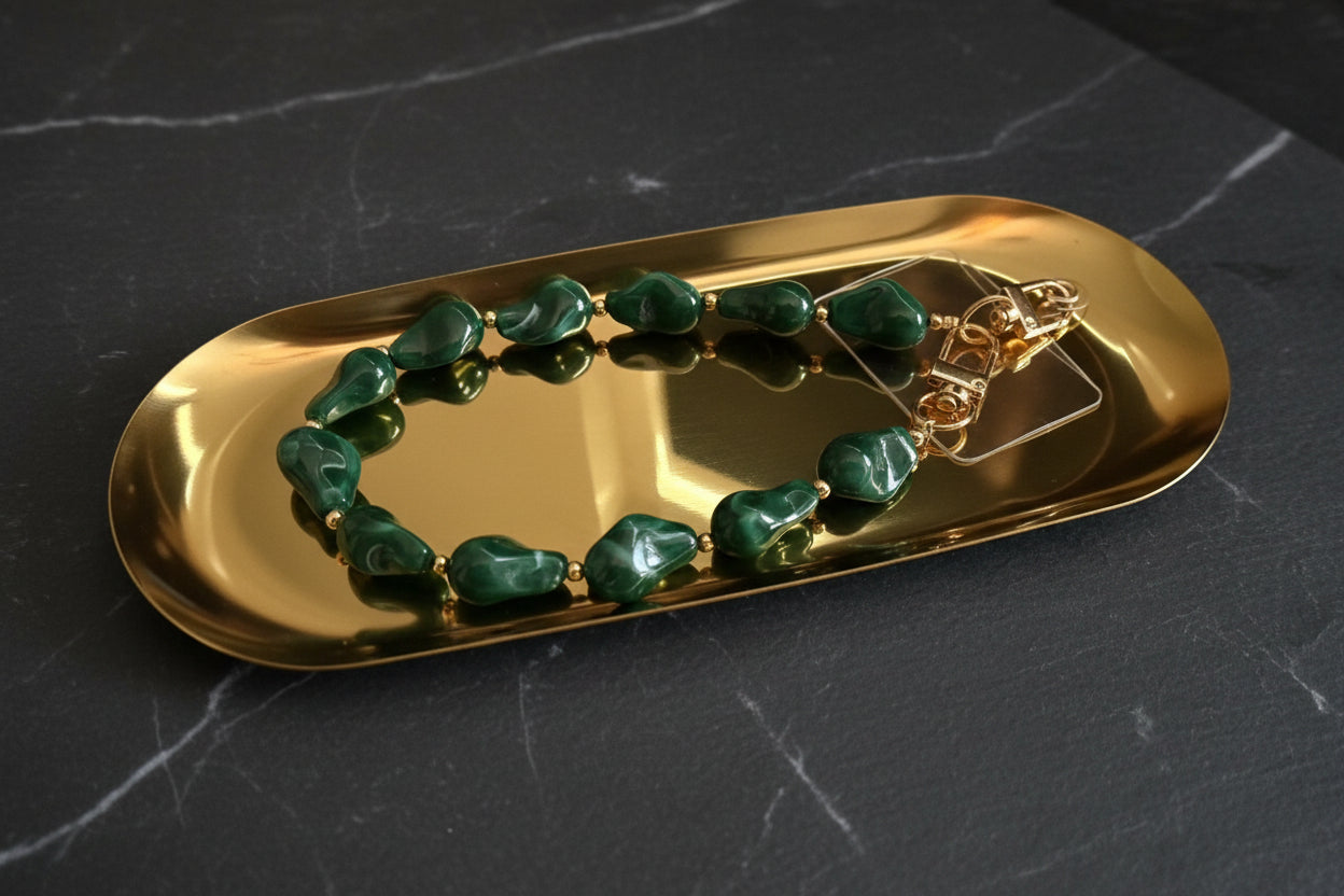 Glow Mystic in Style emerald groen acryl kralen telefoonkoord met gouden details op een gouden glanzende schaal met een zwart marmeren achtergrond.