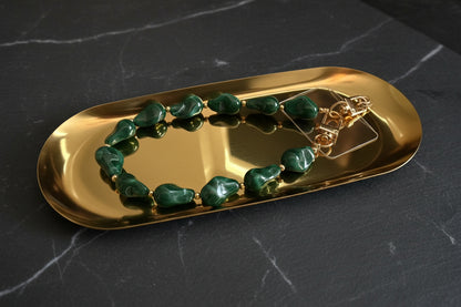 Glow Mystic in Style emerald groen acryl kralen telefoonkoord met gouden details op een gouden glanzende schaal met een zwart marmeren achtergrond.