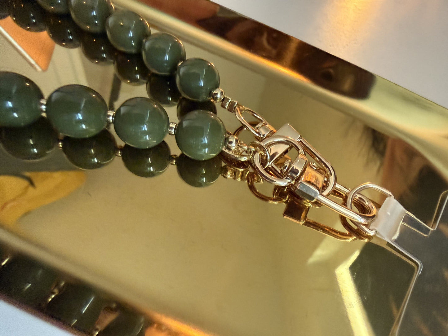 Groene kralen met gouden details telefoonkoord van Glow Mystic in Style op een goudkleurige schaal.