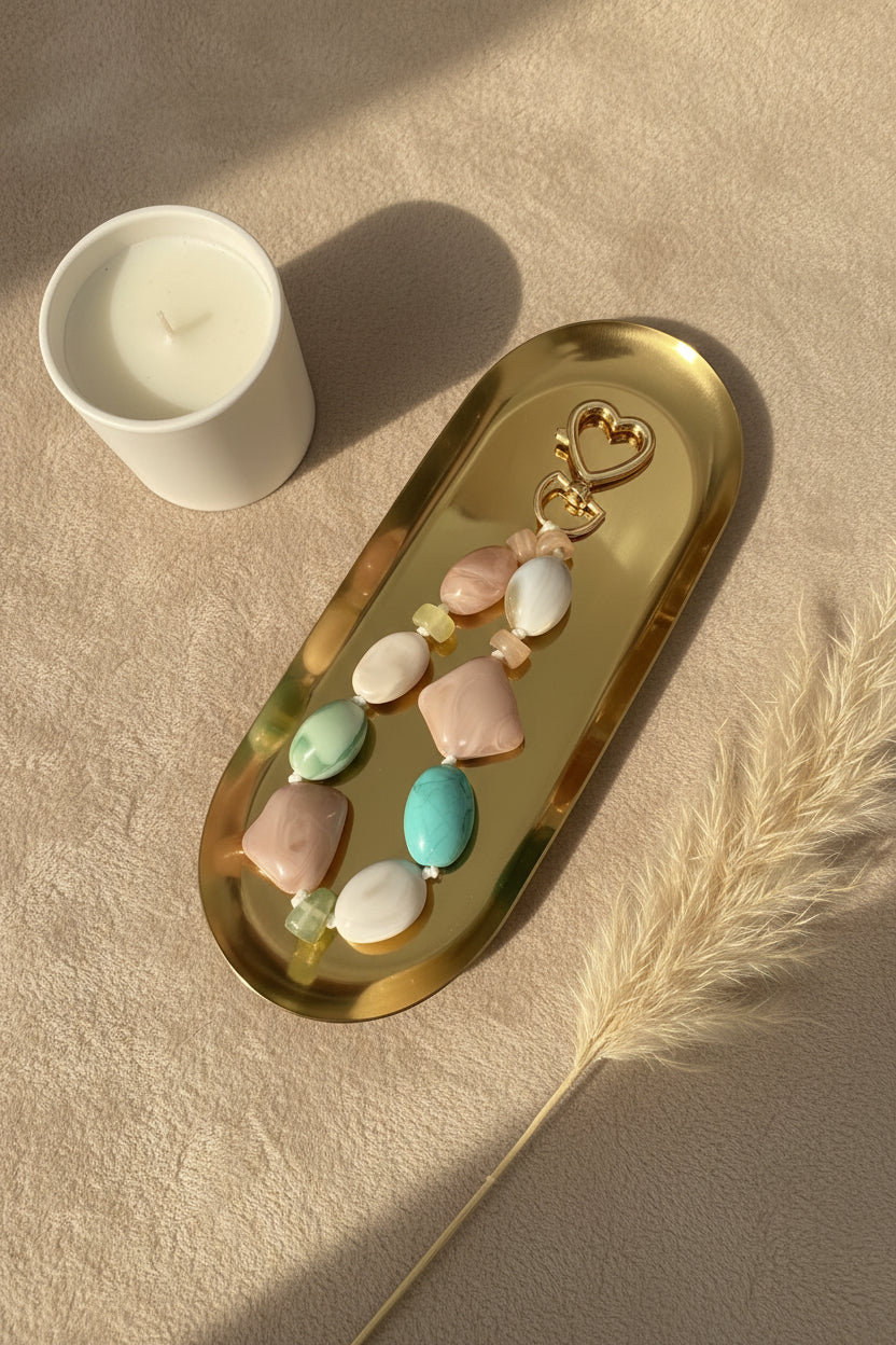 Glow Mystic in Style pastelkleurig acryl telefoonkoord met goudkleurige hartjessluiting op gouden schaal met een beige achtergrond.