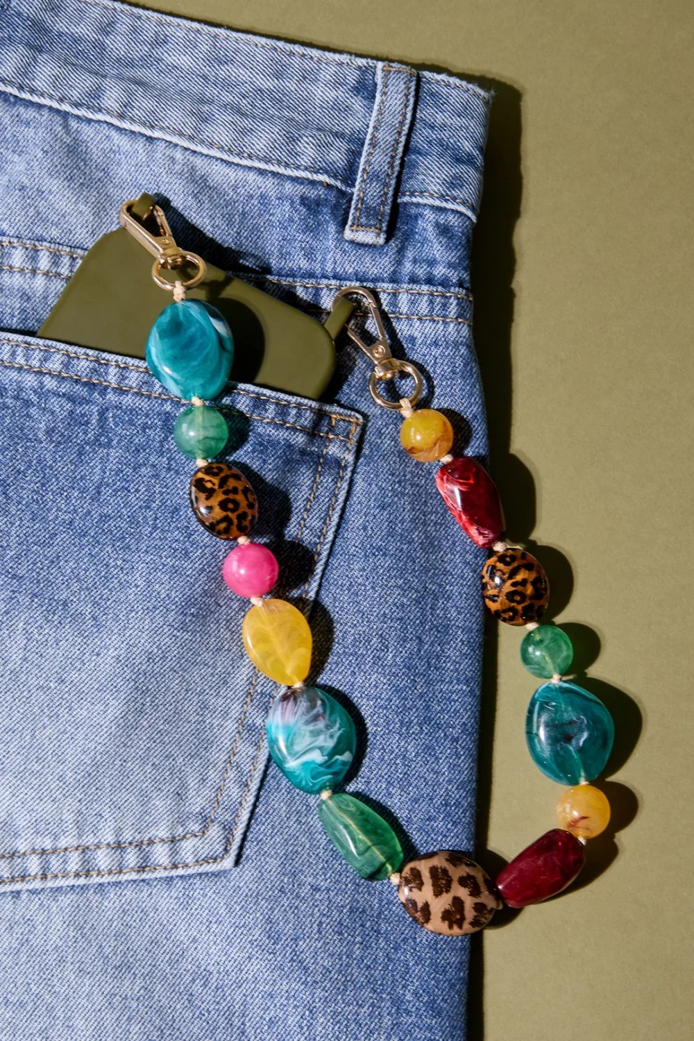Meerkleurige chunky acryl telefoonkoord aan een groene telefoon bevestigd in een broekzak van een jeans.