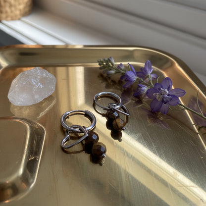Glow Mystic in Style zilveren charm oorbellen met open hartje en bruine kralen op gouden tray