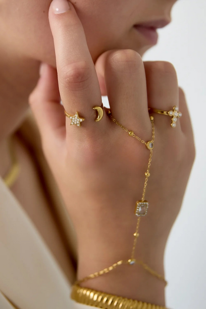 Sfeerbeeld van een hand met goudkleurige sieraden, waarop de verstelbare RVS ster en maan ring Mystic Star elegant om de wijsvinger gedragen wordt.
