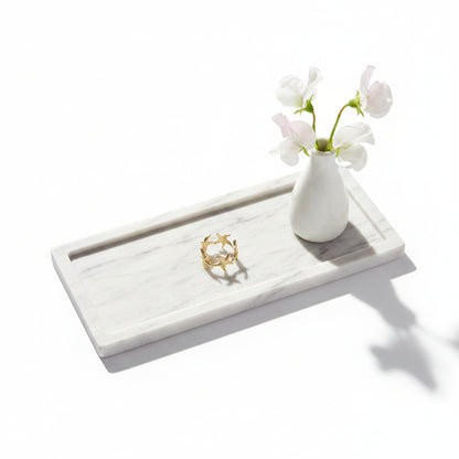 Goudkleurige RVS ring met zeesterren op een rechthoekig marmeren dienblad naast een klein wit vaasje met witte bloemen.