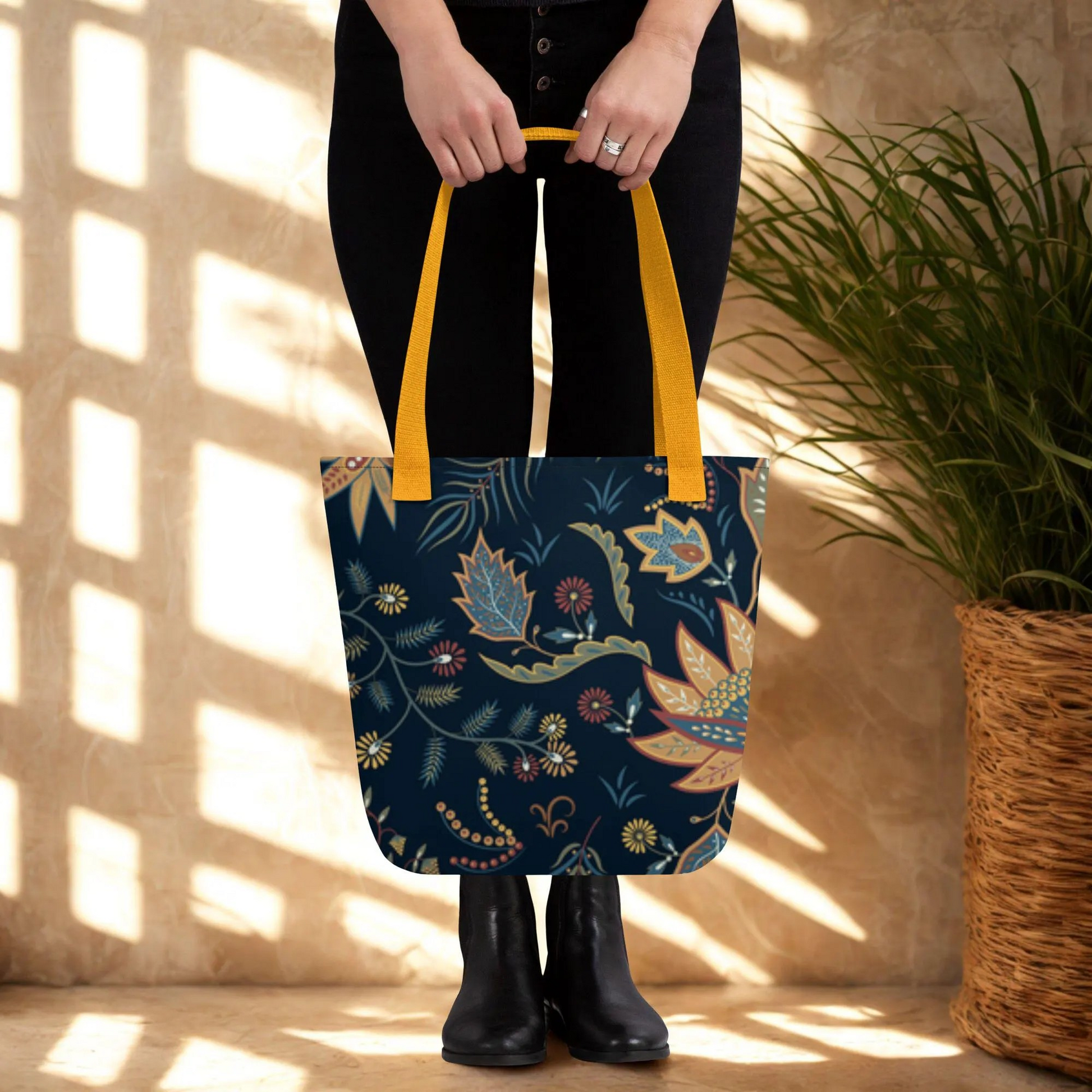 Autumn Floral Tote Bag with dark blue background and colorful fall leaves pattern, featuring yellow handles, held by person wearing black pants and boots.