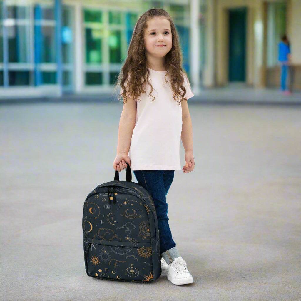 Child standing holding Mystic Moons and Stars Backpack with celestial design featuring moons and stars