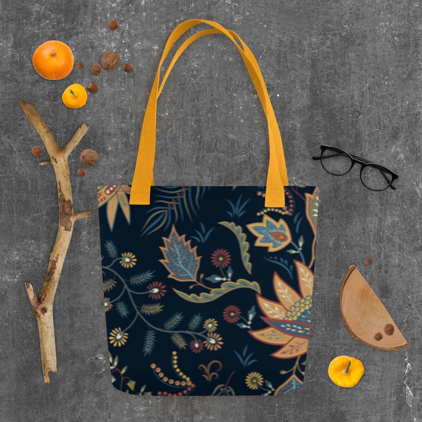 Autumn Floral Tote Bag with navy background and warm floral patterns, featuring sturdy orange handles on gray surface with seasonal decor.