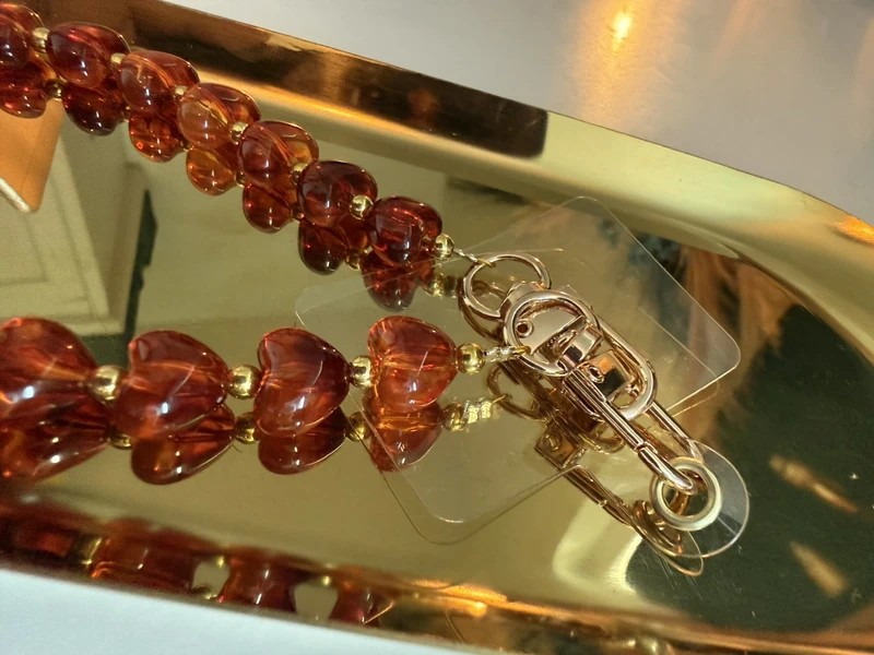 Amberkleurige telefoonkoord met hartjes en gouden details op een goudkleurige schaal.