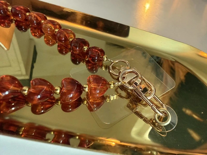 Amberkleurige telefoonkoord met hartjes en gouden details op een goudkleurige schaal.
