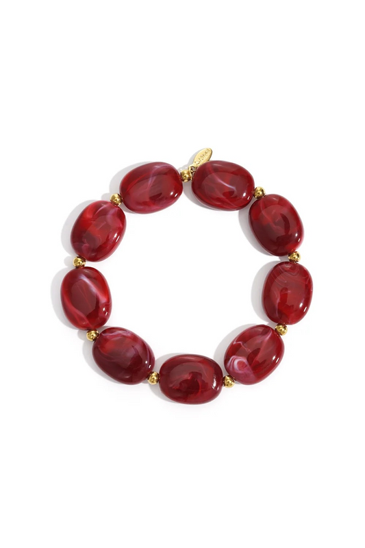 Luxe grove armband van bordeauxrode gemarmerde acryl kralen met kleine goudkleurige tussenkralen op een witte achtergrond.