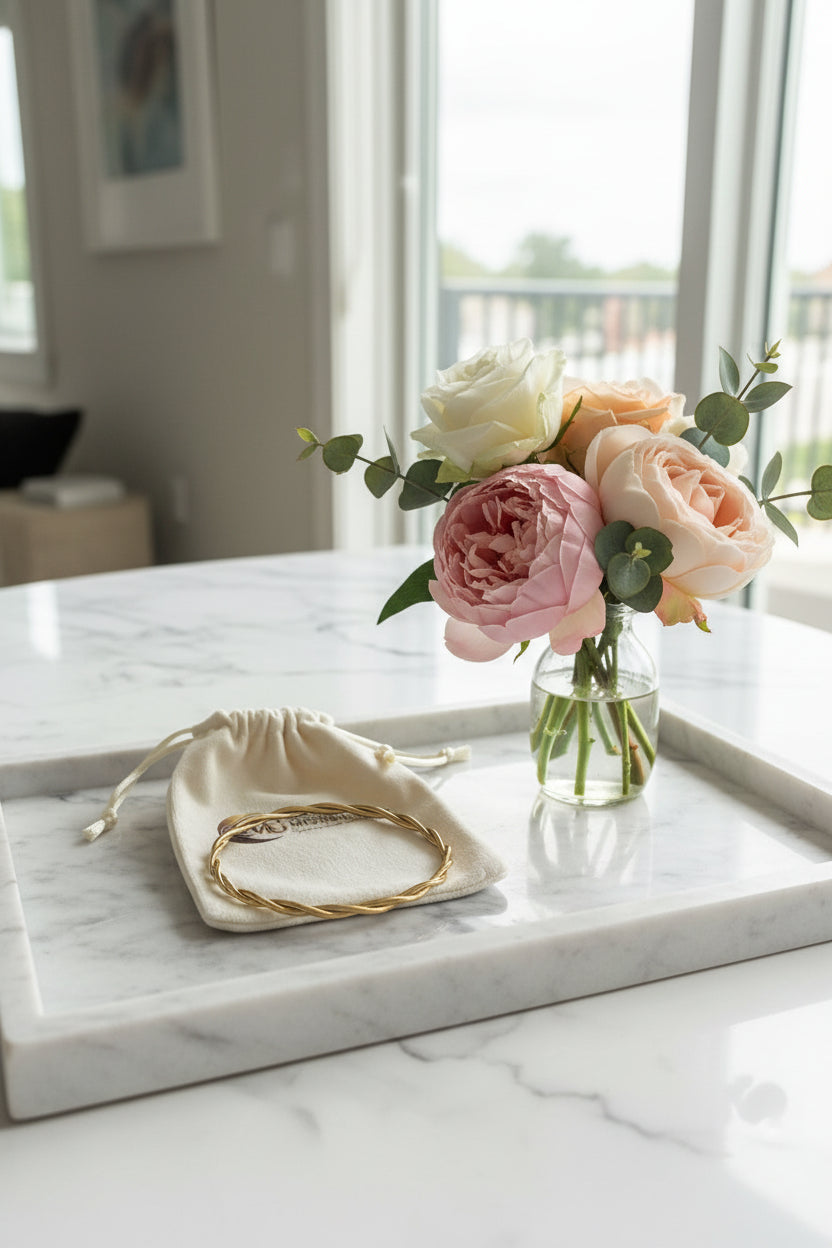 Bangle armband goud rvs gekrulde armband op een marmeren schaal met een vaasje bloemen op de achtergrond