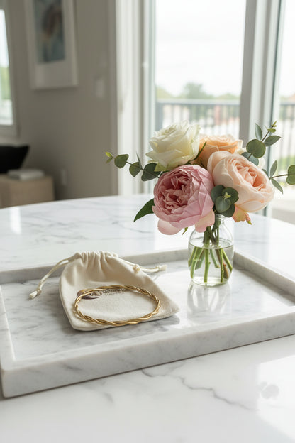Bangle armband goud rvs gekrulde armband op een marmeren schaal met een vaasje bloemen op de achtergrond