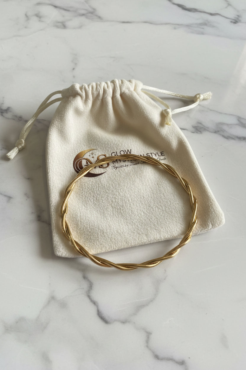 Elegante gouden gekrulde bangle armband liggend op een Glow Mystic in Style sieradenzakje op een wit-grijze marmeren plaat.