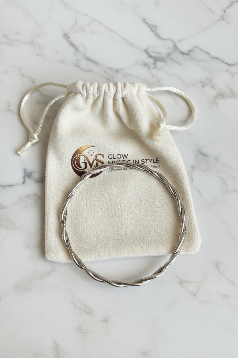 Elegante zilveren gekrulde bangle armband van waterproof RVS liggend op een wit Glow Mystic in Style sieradenzakje op een wit-grijze marmeren plaat.
