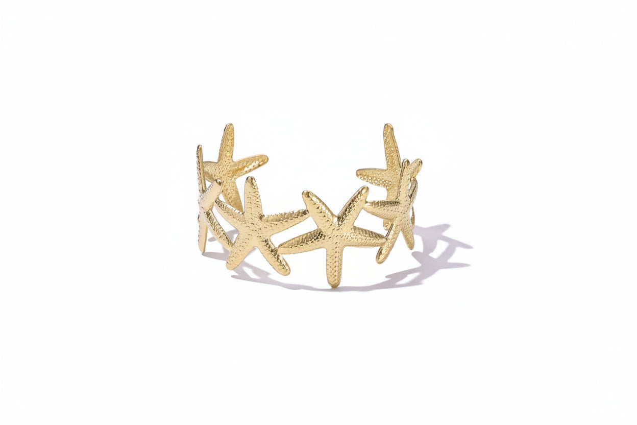 Brede gouden bangle armband van Glow Mystic gemaakt van stainless steel met een gedetailleerd patroon van zeesterren, gefotografeerd op een witte achtergrond.