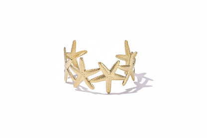 Brede gouden bangle armband van Glow Mystic gemaakt van stainless steel met een gedetailleerd patroon van zeesterren, gefotografeerd op een witte achtergrond.